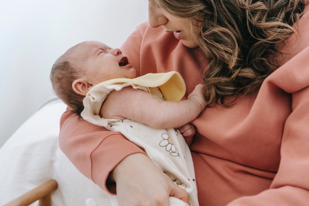 a mother kissing a young baby and holding them on her shoulder