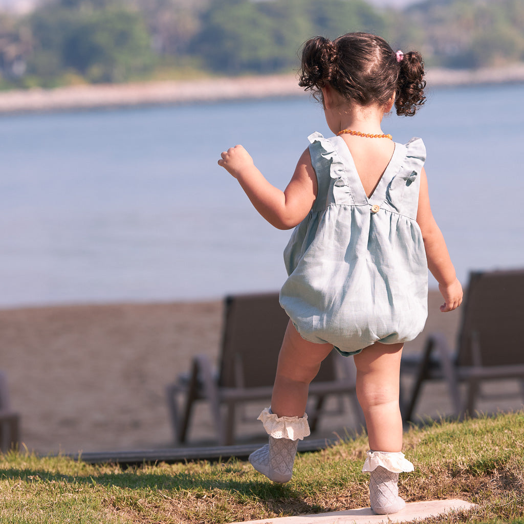 A toddler wearing a Classic Linen Romper by Hiccups and Buttercups